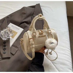 Close-up of cream pillow bag with crocodile texture, metal logo and plush pendant