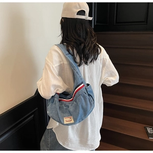 Detail of light blue denim crescent shoulder bag featuring tricolor webbing strap and fabric label