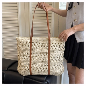Detail of hand-woven straw tote with hollow floral pattern and brown leather strap