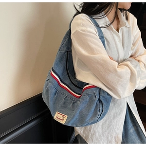 Detail of blue denim crescent bag with tricolor ribbon and brand label on strap