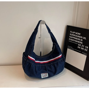 Detail of blue denim hobo bag featuring red and white striped webbing and vintage woven label
