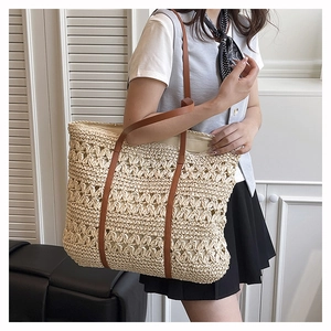 Detail of hollow-out woven pattern and brown leather strap on cream straw tote bag