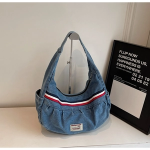 Detail of blue denim tote bag with red and white striped ribbon and metal zipper closure