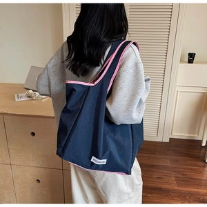 Detail view of large navy nylon tote bag with pink trim worn by model in a home office