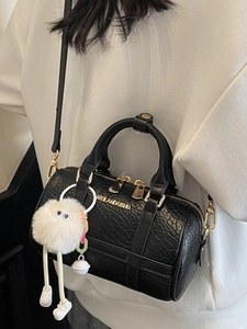 Elegant black embossed leather pillow bag with gold logo and fluffy white charm detail