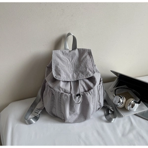 Detail of grey nylon backpack featuring embroidery and side pocket in study scene