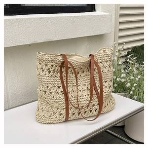 Detailed close-up of hollow woven straw tote with brown leather handles on white bench