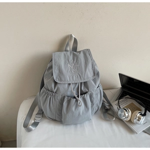 Detail view of a light gray nylon backpack with drawstring closure and laptop accessories