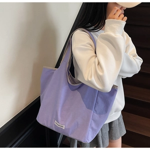 Detail of a large purple canvas tote bag with gray piping and brand label for daily use