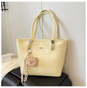 Détail d'un sac cabas jaune gaufré crocodile avec logo en métal et breloque en peluche