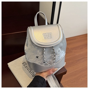 Detail of silver metallic mini backpack featuring patches and stylish metal chain accent