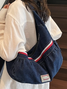 Large blue denim crossbody cloud bag with red strap on wooden stairs model view