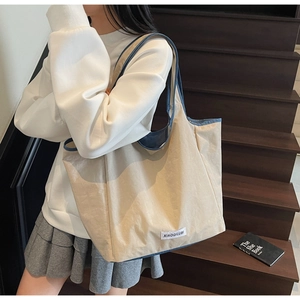 Detailed side view of a large cream tote bag with navy blue trim and long shoulder strap