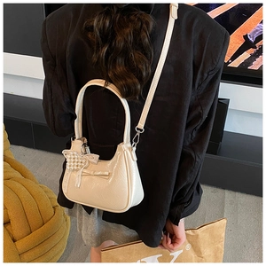 Elegante borsa beige in vernice arricciata con fiocco e ciondolo di perle su modella