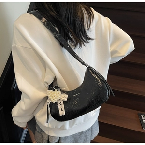 Detail of black patent leather hobo bag with pearl floral lace bow charm and silver logo