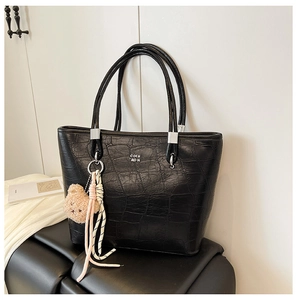Détail d'un sac cabas noir à motif crocodile avec boucles argentées et pendentif ours