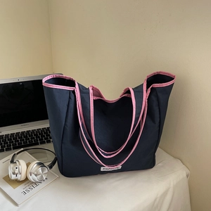 Detail of navy blue tote bag with pink piping, logo patch, and long double handles