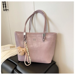 Détail du sac cabas lilas avec texture crocodile, logo en métal et breloque ours