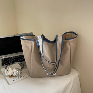 Detail of a large beige canvas tote bag with navy blue trim in a stylish home office setting