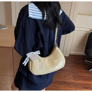 Detail of light yellow baguette bag with pearl lace bow charm on soft leather surface