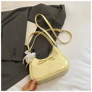 Dettaglio di una borsa giallo pallido con decorazione a fiocco, pendente in pizzo di perle e tracolla