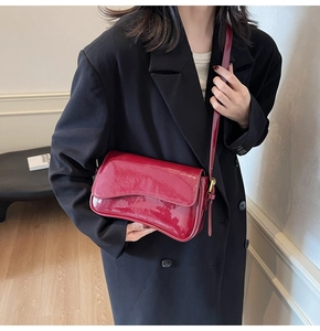 Close-up of red glossy patent leather shoulder bag with gold buckle on a model