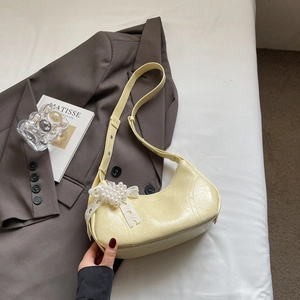 Detail view of cream yellow leather baguette bag with pearl lace bow charm
