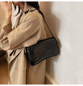 Close-up of black patent leather shoulder bag with golden metal rings on the side