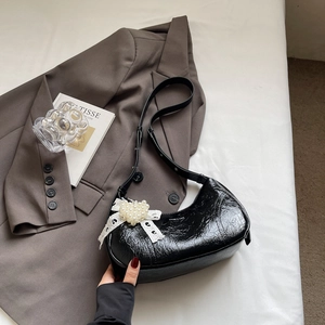 Detail of black pleated patent leather underarm bag with lace bow and pearl heart charm