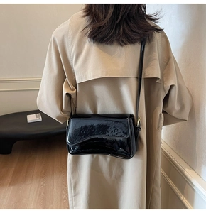 Detailed view of black patent leather shoulder bag with asymmetrical flap and gold hardware