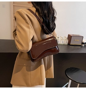 Detail of glossy brown patent leather shoulder bag with flap and slim strap
