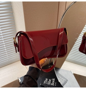 Detail of burgundy patent leather shoulder bag with asymmetric flap and gold metal buckle