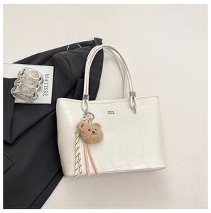 Détail du sac cabas crème avec motif crocodile, pendentif ours en peluche et pompon rayé