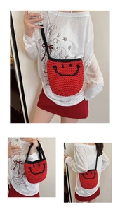 Macro detail of a red knitted bucket bag featuring a hand-woven smiley face and black strap