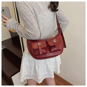 Detail of dark red faux leather crescent bag with dual front pockets and silver buckles
