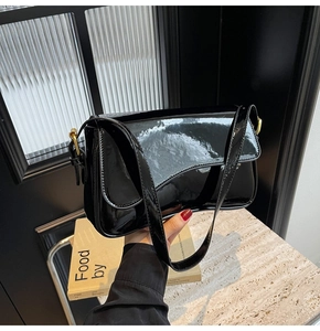 Close-up of black patent leather shoulder bag with asymmetrical flap and gold buckle