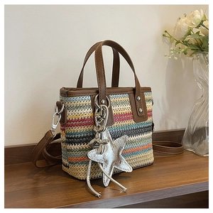Detail of multi-color woven straw bag featuring brown leather trim and star charm accessory