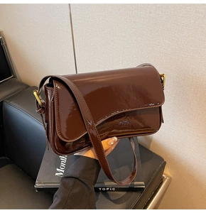 Detail of glossy brown patent leather shoulder bag with gold hardware and flap closure