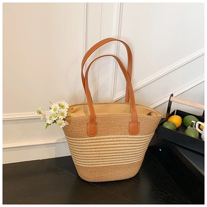 Detail der gewebten Stroh-Tote-Bag mit braunen Ledergriffen und Gänseblümchen-Akzent