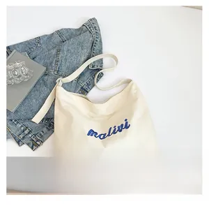 Detailed flat lay of beige canvas tote bag with blue lettering and denim jacket