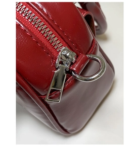 Macro shot of high-gloss red leather texture and silver metal zipper detail on the handbag