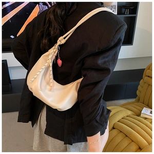 Détail d'un sac demi-lune crème avec décoration tressée et pendentif coeur rose