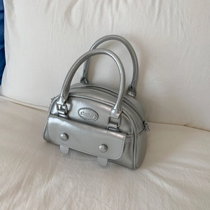 Detailed shot of metallic silver handbag with aimater logo on white fabric background