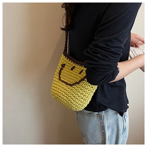 Detail of a bright yellow knitted bucket bag with a brown smiley face on a model shoulder