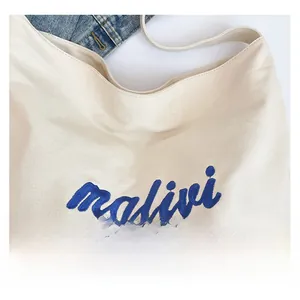 Detail of white canvas tote bag showing blue malivi embroidery and fabric texture