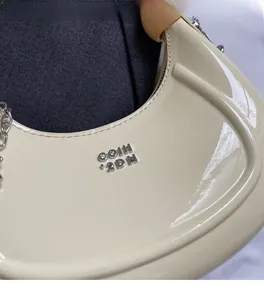 Close-up of cream white patent leather hobo bag with silver metal logo and chain detail