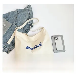 Size comparison of white canvas tote bag with smartphone and denim jacket for scale