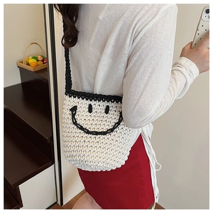 Detail of white knit bucket bag with black smiley face pattern worn by a model in red dress