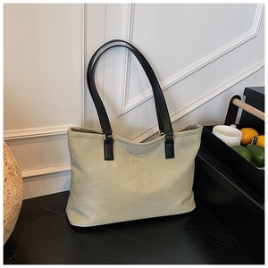 Detail of sage green textured leather tote bag with elegant gold hardware on black wood