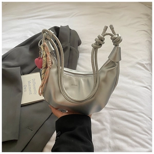 Détail du sac à main argenté en demi-lune avec poignée nouée et breloque cœur